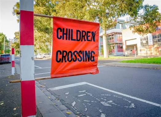 A Children Crossing flag mounted on a red and white pole at a roadside school crossing